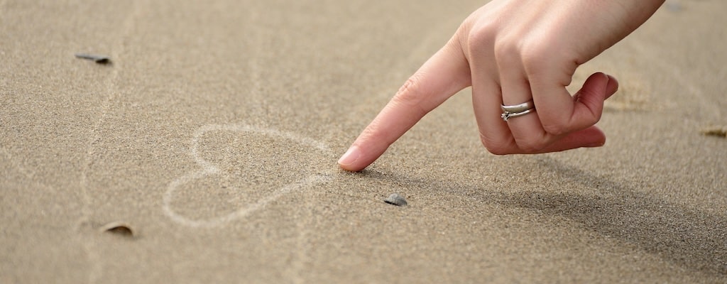 Eine Hand zeichnet ein Herz in den Sand - als Sinnbild für Selbstliebe und Selbstwert Affirmationen 