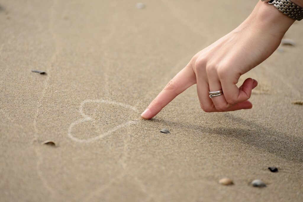 Eine Hand zeichnet ein Herz in den Sand - als Sinnbild für Selbstliebe und Selbstwert Affirmationen